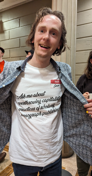 Simon Bowie wears a t-shirt saying 'ask me about overthrowing capitalist practices of scholarly monograph publishing'